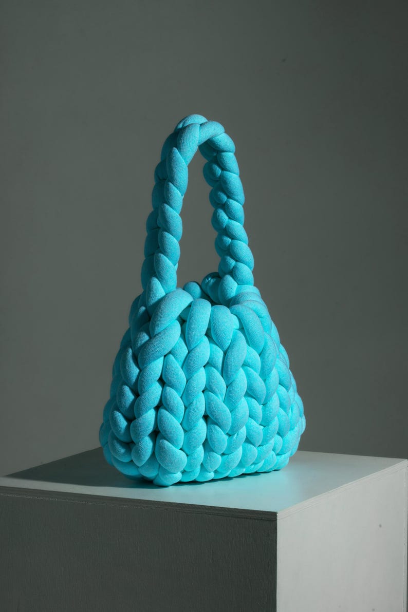 Puede incluir: Un bolso tote de punto azul brillante con un asa trenzada.
