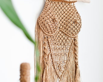 May include: A gold macrame wall hanging with a unique design and fringe details. The hanging is made of natural fibers and has a bohemian aesthetic.