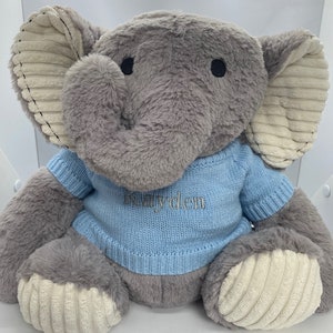 Può includere: Un peluche a forma di elefante grigio con grandi orecchie e un maglione azzurro. Il maglione ha il nome "Kayden" ricamato con filo blu coordinato. Le orecchie e i piedi dell'elefante hanno una consistenza simile al velluto a coste.
