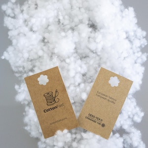 May include: A close-up shot of fluffy white filling material with two brown tags. One tag reads "CottonFast" with a spool and needle graphic. The other tag states "European fabrics, European quality" and "OEKO-TEX STANDARD 100".