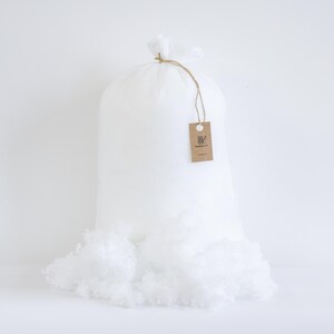 May include: A large white bag filled with fluffy, white polyester fiber. The bag is tied at the top with twine and a small tag. Some of the fiber has spilled out of the bag. The tag has a logo and the text "Cottontail Co."