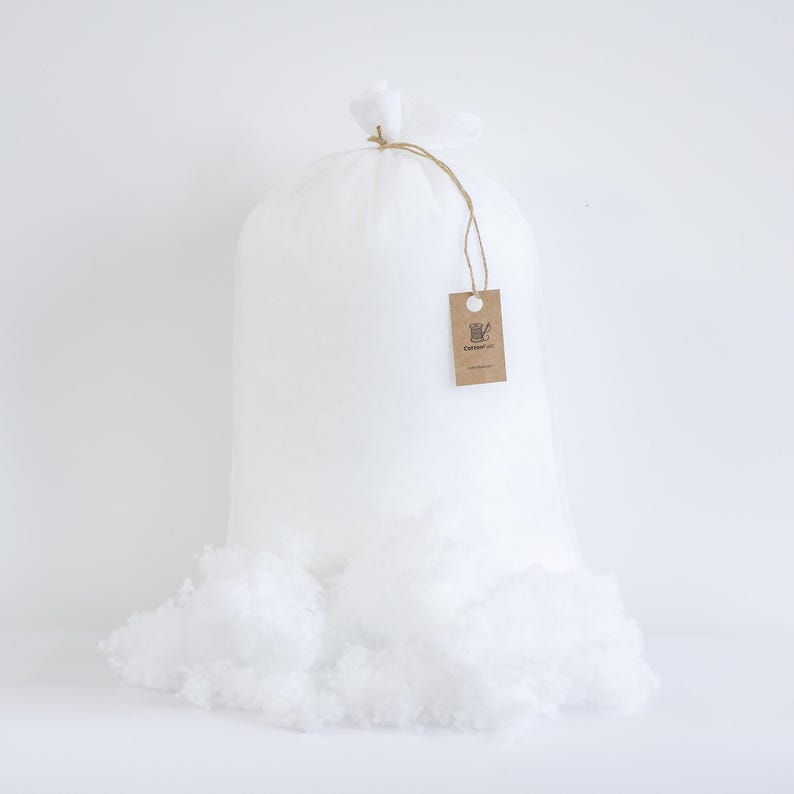 May include: A large white bag filled with fluffy, white polyester fiber. The bag is tied at the top with twine and a small tag. Some of the fiber has spilled out of the bag. The tag has a logo and the text "Cottontail Co."