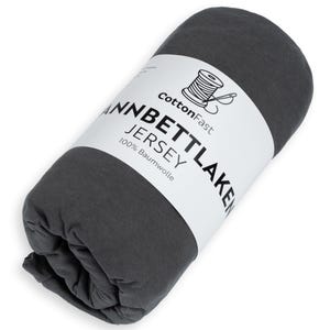 May include: Rolled-up dark grey jersey knit sheet. A white label displays the text "CottonFast" above a spool of thread graphic, and the text "Jannbettlaken Jersey 100% Baumwolle".