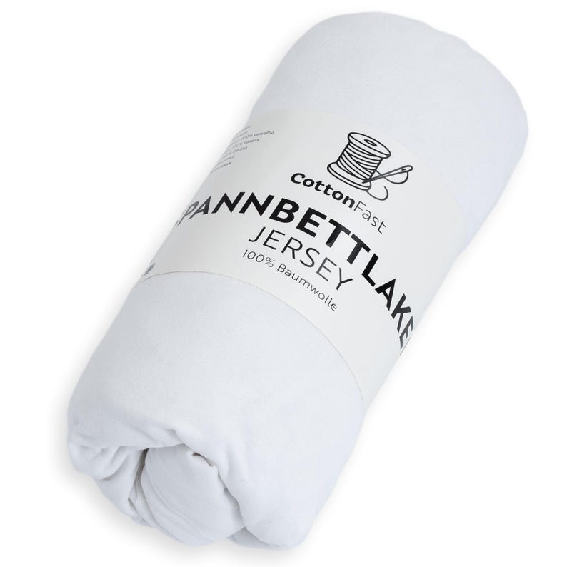 May include: A rolled white fitted sheet with a label. The label reads "CottonFast," "Spannbettlaken Jersey," and "100% Baumwolle." A graphic of a thread spool is also on the label. The sheet is made of jersey.