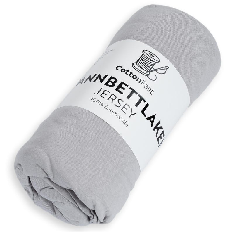 May include: A rolled-up, pale grey jersey knit sheet. A white label wraps around the sheet, displaying the text "CottonFast", a spool and needle graphic, and the words "WANNBETTLAKEN JERSEY 100% Baumwolle".