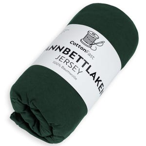 May include: A rolled-up, dark green jersey sheet. The product is wrapped with a white label that reads "CottonFast" and "Jannbettlaken Jersey 100% Baumwolle". A graphic of a spool of thread is also on the label.
