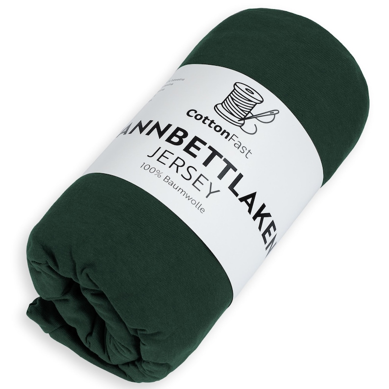 May include: A rolled-up, dark green jersey sheet. The product is wrapped with a white label that reads "CottonFast" and "Jannbettlaken Jersey 100% Baumwolle". A graphic of a spool of thread is also on the label.