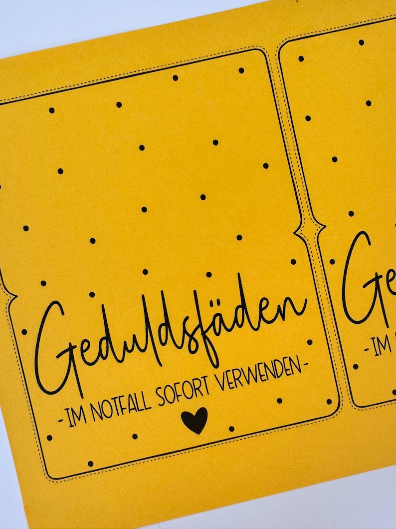 K&ouml;nnte beinhalten: Nahaufnahme einer gelben Karte mit schwarzem Text und einem Herz. Die Karte lautet "Geduldsf&auml;den - IM NOTFALL SOFORT VERWENDEN -" in einer handschriftlichen Schriftart. Kleine schwarze Punkte sind &uuml;ber die Oberfl&auml;che der Karte verstreut.