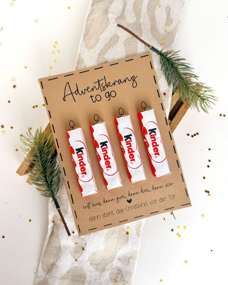 May include: A brown card with the text "Adventskranz to go" and four Kinder chocolate bars arranged to look like candles. The card has the text "erst eins, dann zwei, dann drei, dann vier, dann steht das Christkind vor der T&uuml;r".
