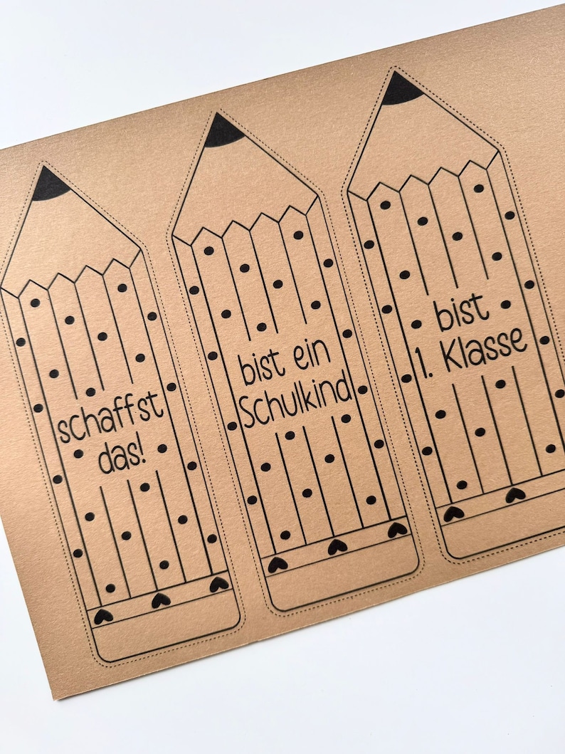 May include: Three brown paper pencil-shaped bookmarks with black outlines and polka dots. The bookmarks have the text "schafft das!" on the left, "bist ein Schulkind" in the middle, and "bist 1. Klasse" on the right.