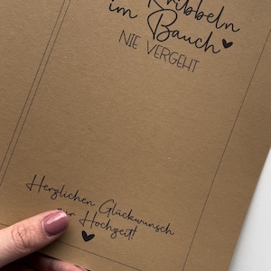 May include: A brown card with black text that reads "DAMIT das Kribbeln im Bauch NIE VERGEHT" and "Herzlichen Gl&uuml;ckwunsch zur Hochzeit!" with a small heart symbol next to each phrase.