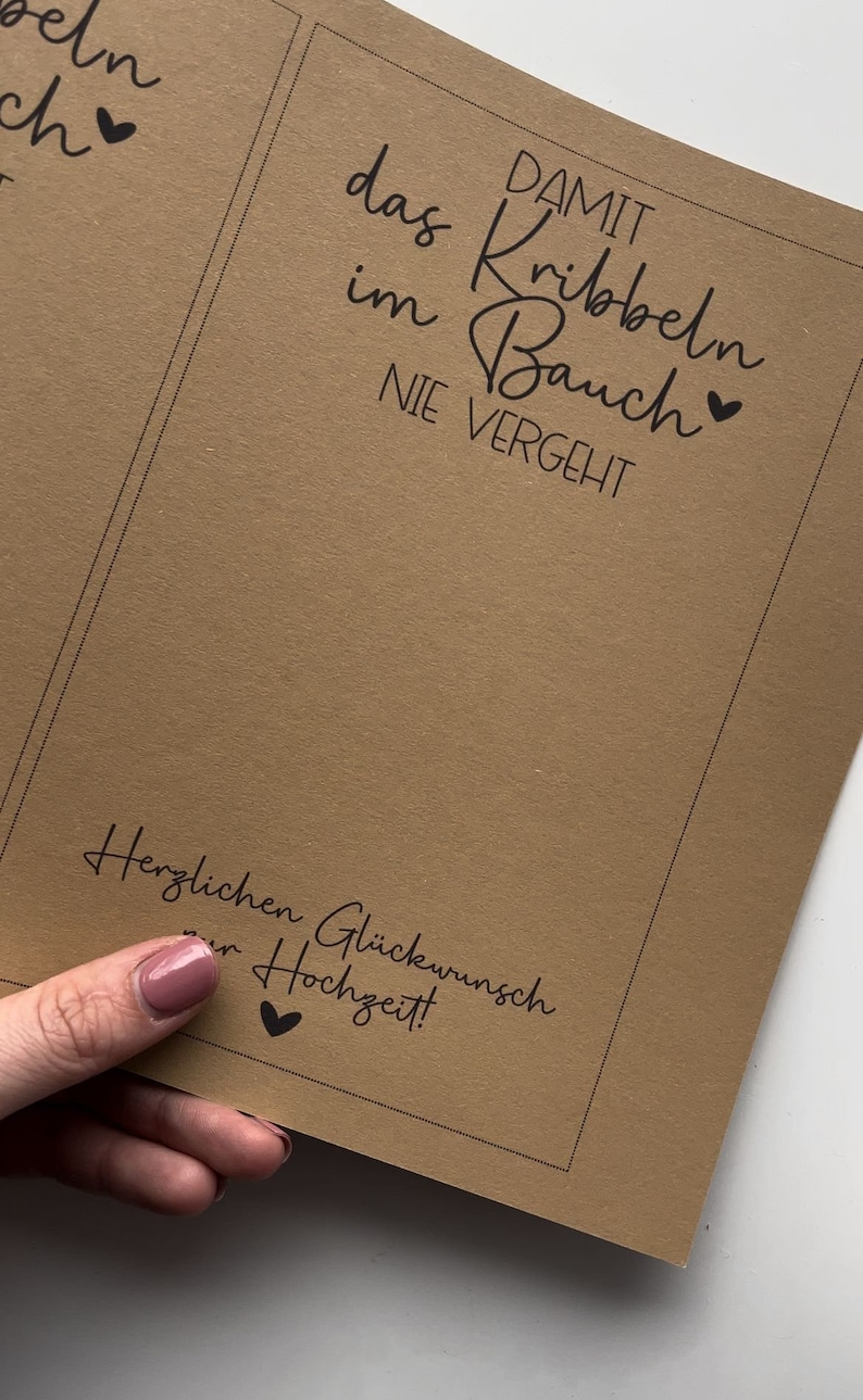 May include: A brown card with black text that reads "DAMIT das Kribbeln im Bauch NIE VERGEHT" and "Herzlichen Gl&uuml;ckwunsch zur Hochzeit!" with a small heart symbol next to each phrase.