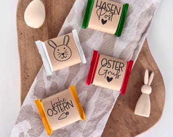 May include: Three small wrapped chocolate bars with Easter-themed designs. The bars are wrapped in brown paper with colorful borders and feature bunny illustrations and text in German. The text on the bars reads "Hasen Post", "Oster Gruss", and "Frohe Ostern".
