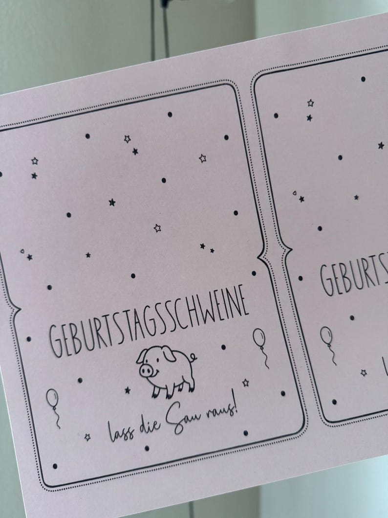 May include: A light pink card with black text and illustrations. The card features the words "GEBURTSTAGSSCHWEINE" and "lass die Sau raus!" along with a pig illustration, stars, balloons, and dots.