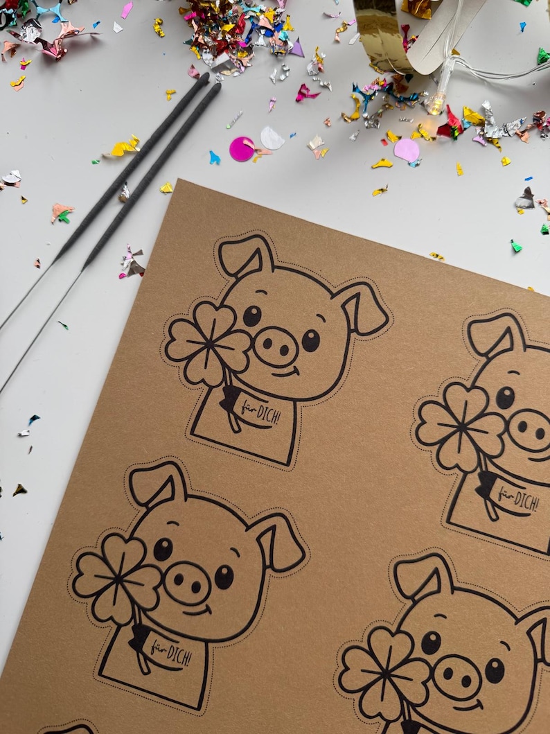 K&ouml;nnte beinhalten: Ein braunes Papier mit mehreren schwarz-wei&szlig;en Schweineaufklebern, die jeweils ein vierbl&auml;ttriges Kleeblatt und den Text "f&uuml;r DICH!" halten. Zwei Wunderkerzen und bunte Konfetti sind um das Papier verstreut.