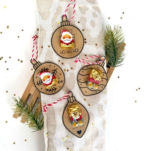 May include: Christmas ornament set featuring Santa Claus and teddy bear designs. Each ornament is crafted from brown cardstock and adorned with a red and white string for hanging. The ornaments have the text "HO HO HO!" and "Fishes list!"