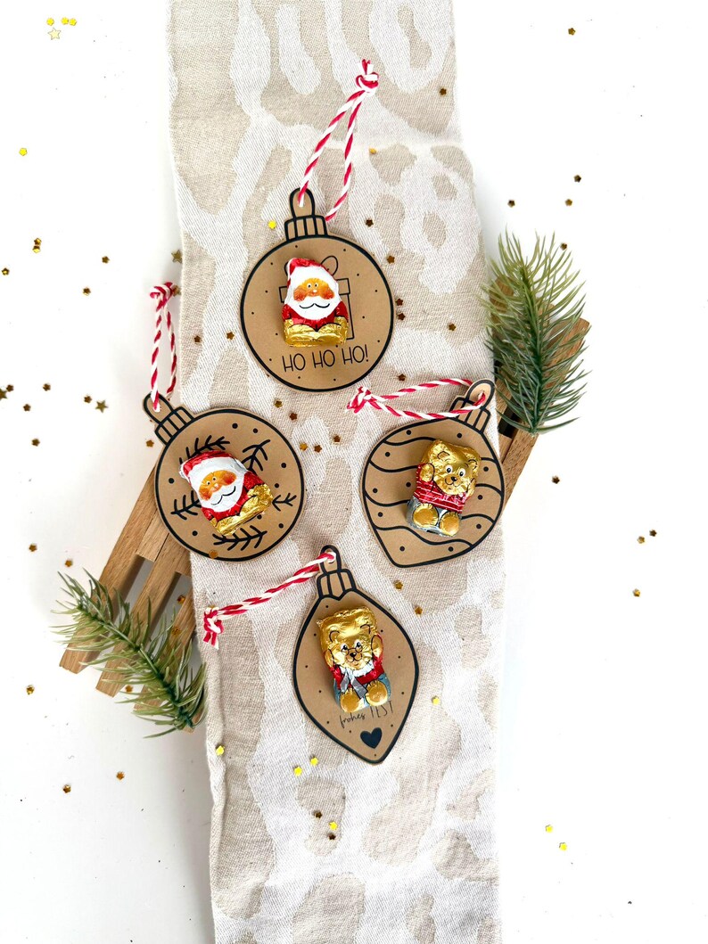 May include: Christmas ornament set featuring Santa Claus and teddy bear designs. Each ornament is crafted from brown cardstock and adorned with a red and white string for hanging. The ornaments have the text "HO HO HO!" and "Fishes list!"