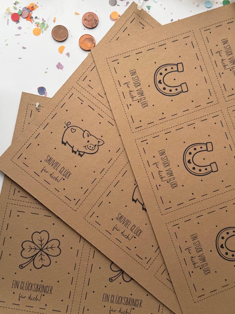 May include: A stack of brown paper cards with black line drawings of a horseshoe, pig, and four-leaf clover. The cards have text in German. Confetti and coins are scattered around the cards.