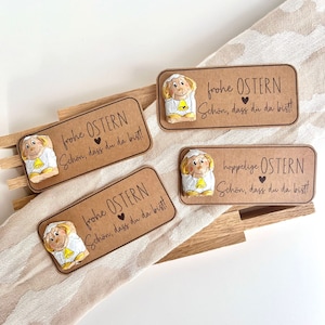 Könnte beinhalten: Vier braune Karton-Etiketten mit jeweils einer weißen Lammfigur. Die Etiketten tragen den Text "frohe OSTERN" und "Schön, dass du da bist!" mit einem Herzsymbol. Ein Etikett trägt den Text "hoppelige OSTERN" anstelle von "frohe OSTERN".