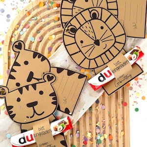 May include: Brown paper animal-shaped birthday cards with black outlines, featuring a tiger and lion design. Each card holds a small chocolate bar with German text. Colorful confetti surrounds the cards on a wooden surface.