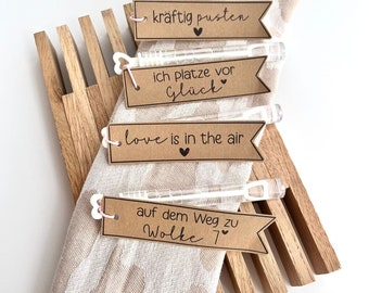 May include: Four brown paper tags with black text and pink hearts attached to clear plastic bubble wands. The tags read "kräftig pusten", "ich platze vor Glück", "love is in the air", and "auf dem Weg zu Wolke 7".