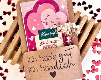 May include: A brown paper gift bag with a pink and white heart-shaped pouch inside. The pouch has a cartoon heart design and the text "Kneipp Lieblings-Mensch". The gift bag has the text "ich hab's gut ich hab dich" and a small heart.