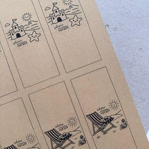 May include: Brown paper bookmarks with black line art illustrations. Designs include a sandcastle, a starfish, a beach chair, and a smiling sun. The text "sch&ouml;ne FERIEN" is printed on each bookmark.