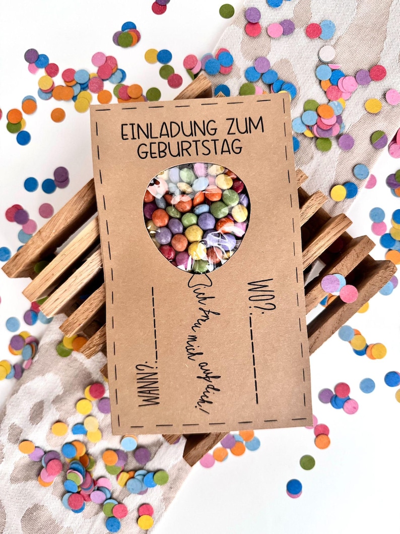 Pode incluir: Um cart&atilde;o castanho com o texto "Einladung zum Geburtstag" e um buraco em forma de cora&ccedil;&atilde;o cheio de doces coloridos. O texto "WANN?" e "WO?" est&aacute; escrito no cart&atilde;o. O cart&atilde;o est&aacute; rodeado de confeti coloridos.