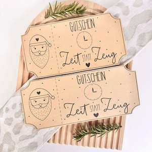 May include: Two brown gift certificates with a Santa Claus illustration and the text "GUTSCHEIN Zeit statt Zeug". The certificates are on a wooden board with a sprig of rosemary.