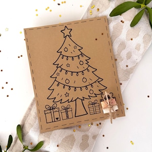 Könnte beinhalten: Eine braune Weihnachtskarte mit einer schwarzen Strichzeichnung eines geschmückten Baumes und Geschenken. Die Karte liegt auf einem gemusterten Stoff mit Mistelzweigen und goldenem Konfetti.