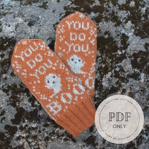 Könnte beinhalten: Ein Paar orangefarbene und weiße Strickhandschuhe mit einem Geist und dem Text "You Do You" darauf. Die Handschuhe liegen auf einer braunen, felsigen Oberfläche. Der Text "Knitting Pattern PDF Only Made by Kisucraft" befindet sich auf einem weißen Kreis.