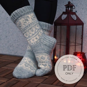 May include: A pair of blue and white knitted socks with a geometric pattern. The socks are worn by a person standing on a wooden floor. A red lantern with heart cutouts is in the background. The text "Knitting Pattern PDF Only Made by Kisucraft" is on a white circle.