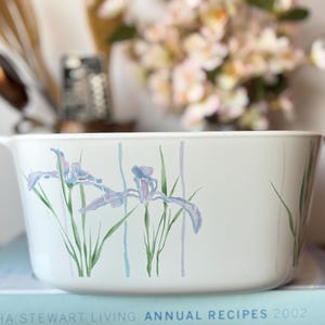 May include: White rectangular casserole dish with handles, decorated with watercolor-style iris flowers in shades of purple and blue. The dish is resting on a book titled "Martha Stewart Living Annual Recipes 2002".