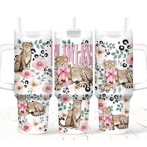 May include: White tumbler with a handle, featuring a cheetah design with pink bows, flowers, and the word "Flawless" in pink. The tumbler has a white lid and a straw.