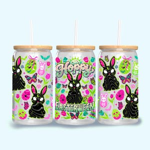 May include: Three glass tumblers with wooden lids and straws. Each tumbler features a colorful design with a black bunny, butterflies, flowers, and the text "Hoppy Easterween". The design includes pink, green, and white elements.