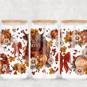 May include: Three glass tumblers with wooden lids and straws. Each tumbler features a fall-themed design with pumpkins, sunflowers, autumn leaves, and a Highland cow. The designs are in shades of orange, brown, and white.