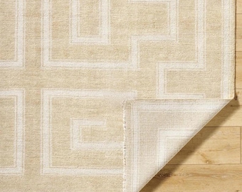 Può includere: Tappeto beige e bianco a motivi geometrici. Il tappeto presenta un motivo a chiave greca ripetuto in bianco su sfondo beige. Un angolo del tappeto è ripiegato, rivelando il lato inferiore. Il tappeto è realizzato in un materiale tessuto.