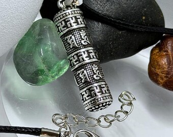 May include: A silver-toned cylindrical pendant featuring embossed geometric patterns and script symbols, suspended on a black cord necklace with a silver-colored metal lobster clasp and an adjustable chain link extension for length customization.