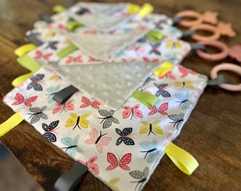 May include: A set of baby sensory toys with a white fabric with colorful butterfly patterns, grey and white fabric with polka dots, and wooden rings with different colors.