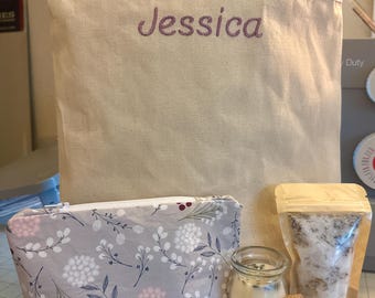 May include: A beige tote bag embroidered with the name "Jessica" in purple, a gray floral print cosmetic bag, a small glass jar with a candle, a cork, and a clear bag with contents.