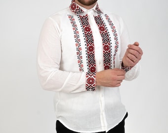 May include: A white long-sleeved shirt with red and black embroidered details. The shirt has a button-up front and a collar.
