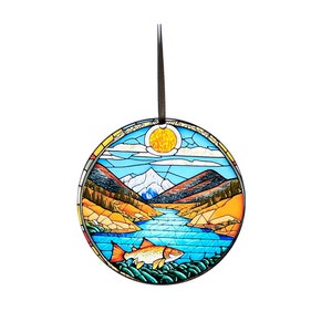 May include: A stained glass ornament depicting a mountain landscape with a river, a sun, and a fish. The ornament is round and has a black metal hanger.