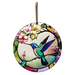 May include: A stained glass style ornament featuring a hummingbird with blue, green, and purple wings, perched on a branch with pink and white flowers.