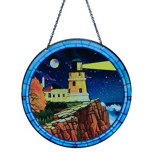 May include: Round stained glass panel depicting a lighthouse scene at night. The lighthouse is yellow with a black top, set against a starry blue sky. A chain is attached for hanging. The panel is framed with a blue border.