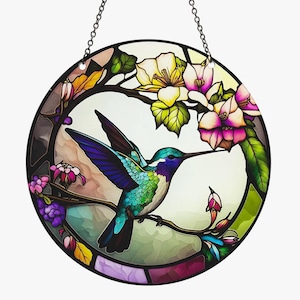 May include: A stained glass window hanging with a colorful hummingbird in flight, surrounded by pink and white flowers with green leaves.