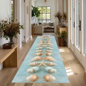 Peut inclure: Un long tapis rectangulaire avec un fond bleu clair présentant un motif de coquillages et d'étoiles de mer. Les coquillages sont dans des tons de beige et de blanc, et les étoiles de mer sont de couleur beige clair. Le tapis est placé dans un couloir.