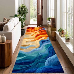 May include: A long, rectangular rug with an abstract design. The rug features a vibrant color palette, with a gradient of orange, yellow, and blue hues. The design resembles flowing waves or brushstrokes, adding a dynamic element to the floor covering.