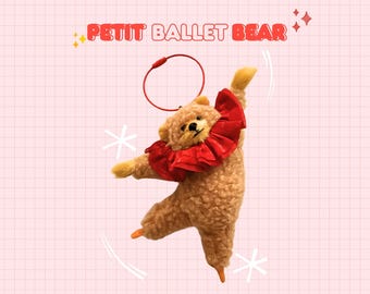 Könnte beinhalten: Ein Plüschteddybär in Ballettpose, mit rotem Rüschenkragen und orangefarbenen Ballettschuhen. Der Bär hat eine rote Schlaufe zum Aufhängen und den Text "PETIT BALLET BEAR" in Rot. Der Hintergrund ist ein rosa Gitter.