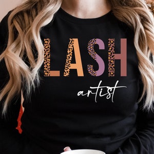 May include: Black long-sleeved shirt with the text "LASH artist" in pink, orange, and brown with a leopard print pattern.