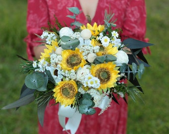 Pode incluir: Um buquê de noiva com girassóis, flores brancas e folhas de eucalipto. O buquê é amarrado com uma fita branca.